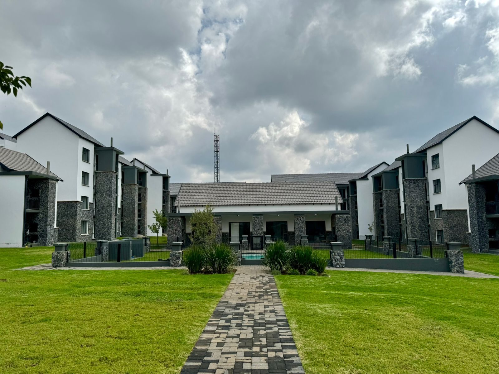 White three-storey apartment blocks with dark stone pillars around a lawn and a paved path
